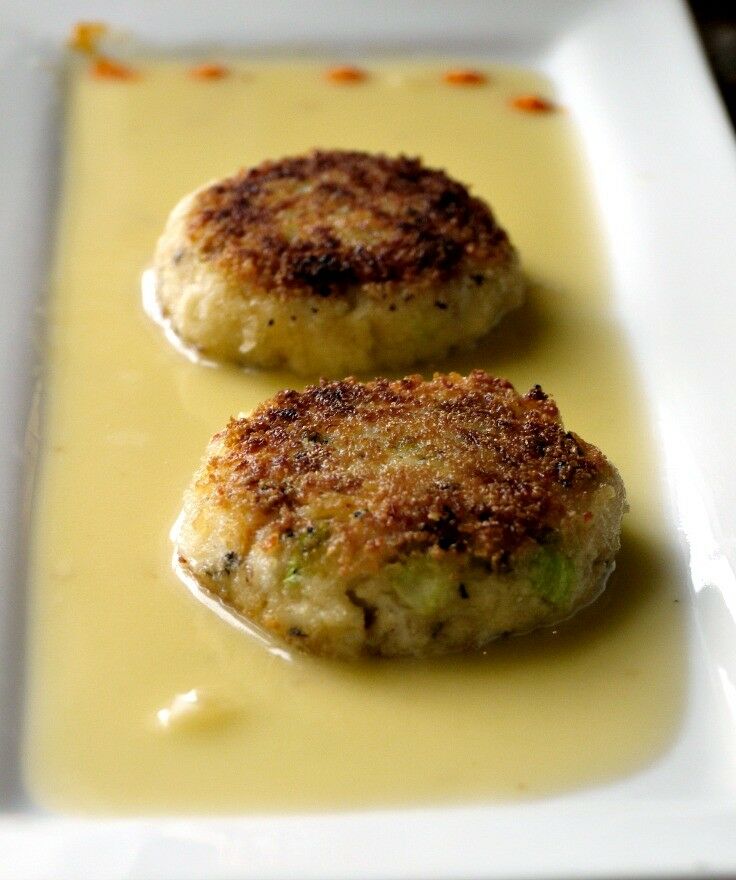 Two crab cakes on a rectangular plate, atop white wine sauce. 