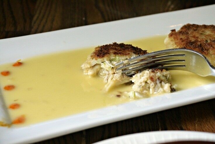 Crab cake, mostly eaten, with a fork cutting off another bite. 