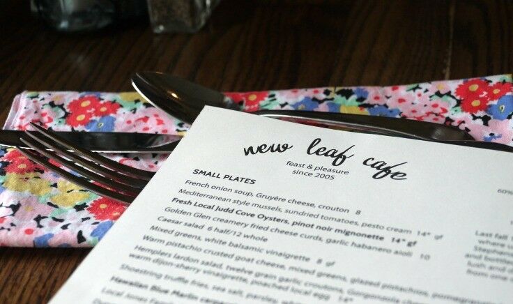 Close-up of the New Leaf Cafe menu, featuring small plates, with silverware service on a brightly colored, flowered napkin. 