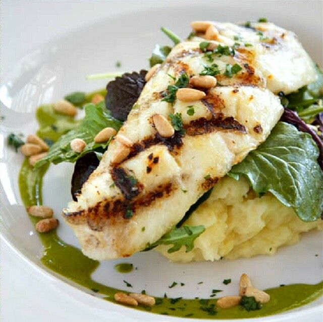 Grilled halibut with crosshatched grill marks, garnished with pine nuts, atop mashed potatoes. 