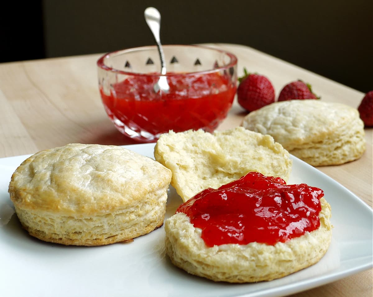 Biscuits and strawberry jam, with a small glass bowl of jam in the background. 