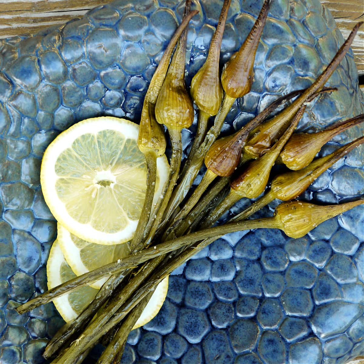 Roasted garlic spears on a highly textured plate, with lemon slices.