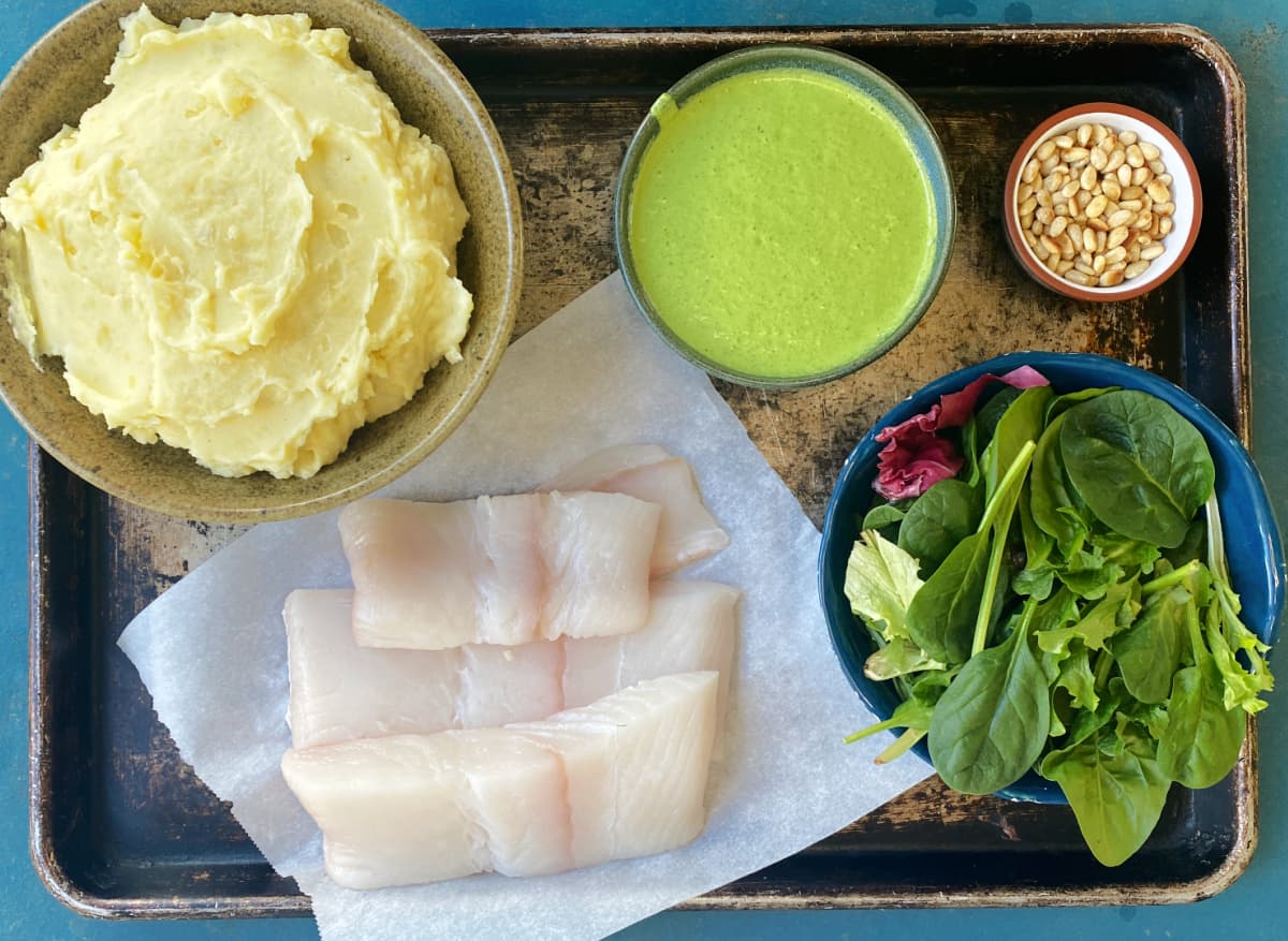 Elements of this recipe displayed on a baking sheet: halibut, mashed potatoes, greens, vinaigrette, and pine nuts.