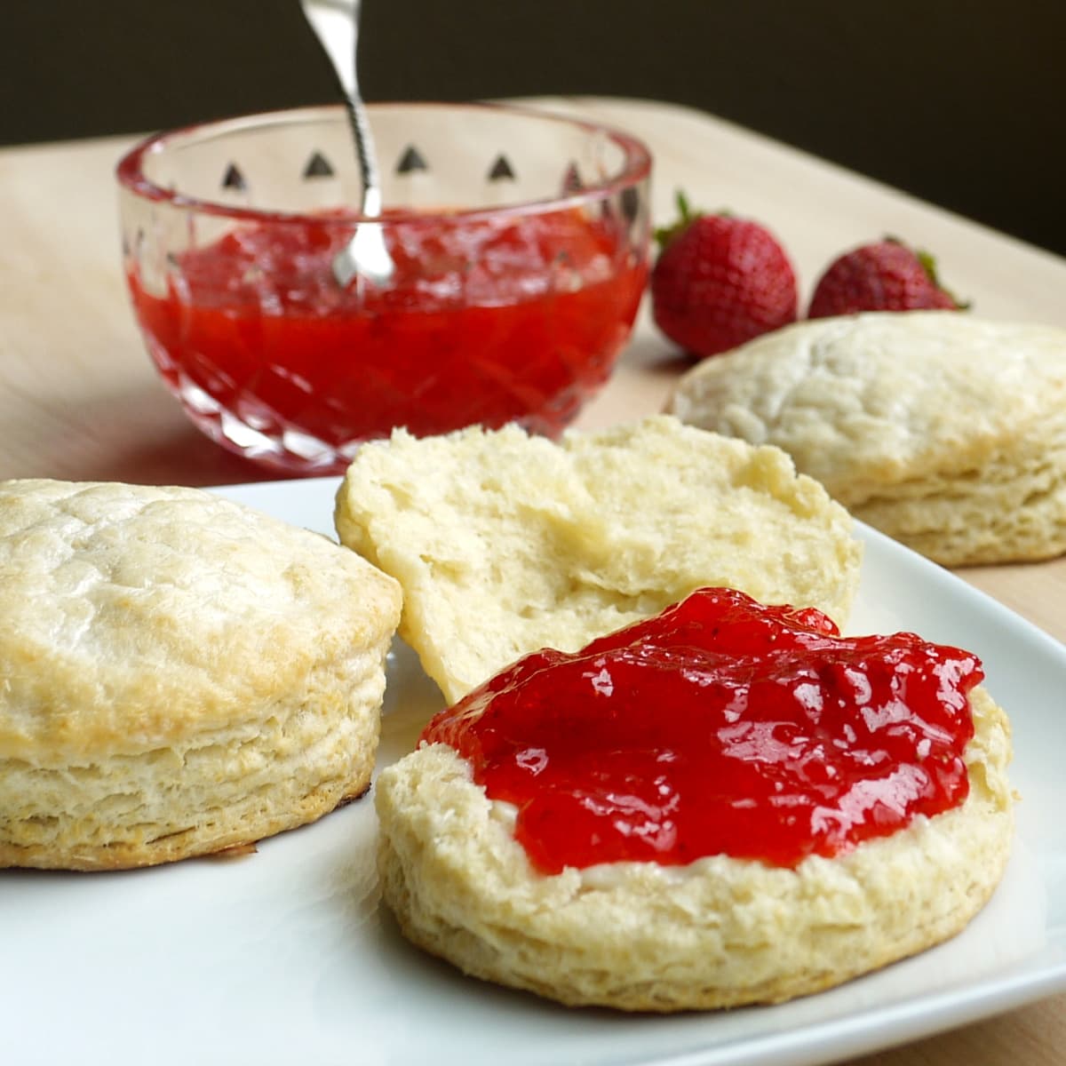 Biscuits and strawberry jam, with a small glass bowl of jam in the background.