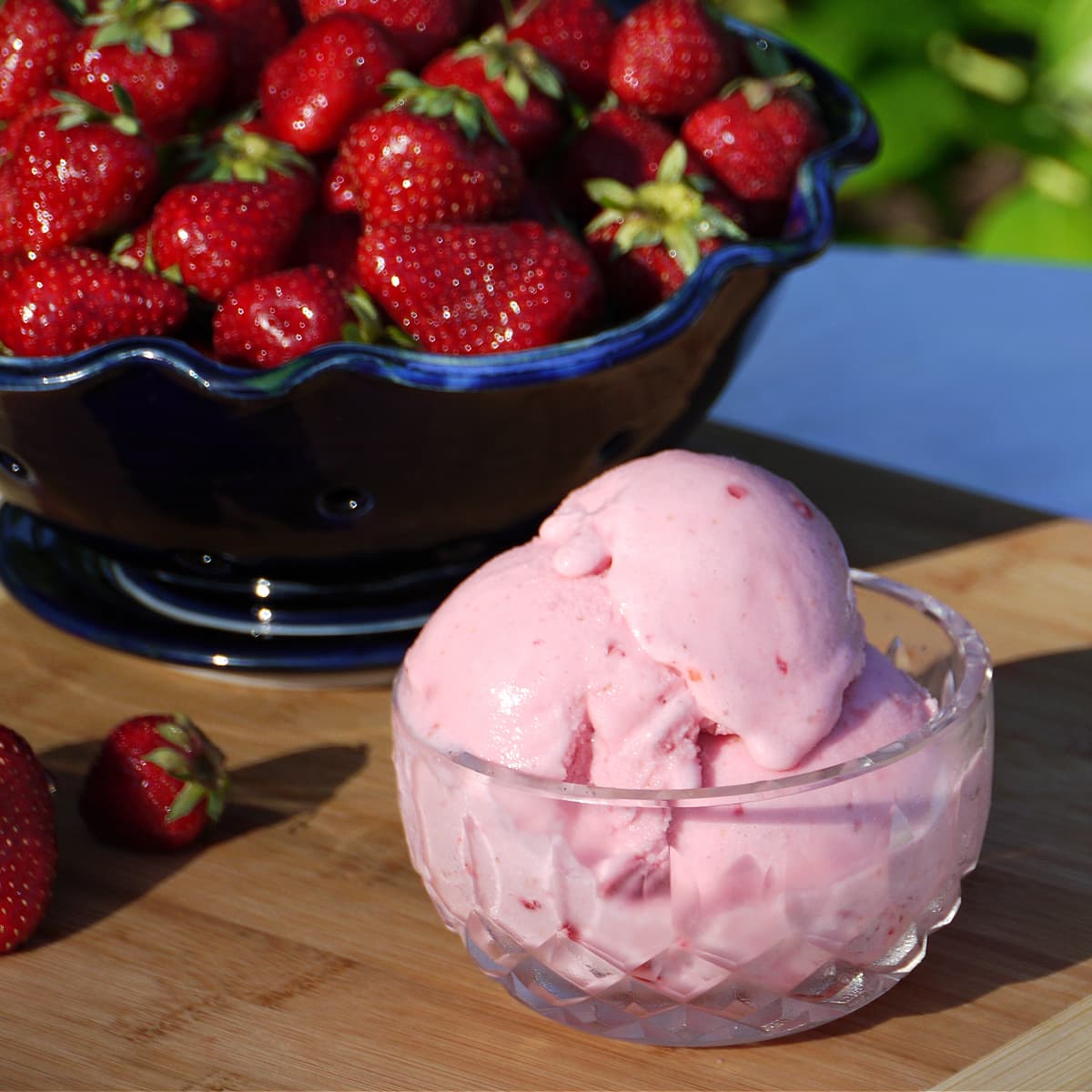 Small glass bowl filled with strawberry ice cream. Berry bowl filled with fresh strawberries in the background. 