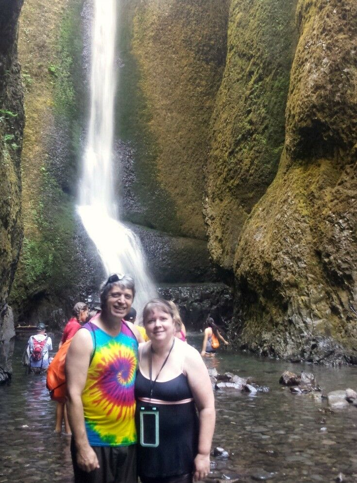 Adorqable middle-aged couple standing in front of a waterfall at the bottom of a large crevasse.  