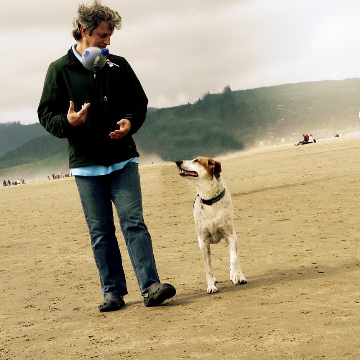 Man with ball and dog watching ball as they walk down the beach together. 