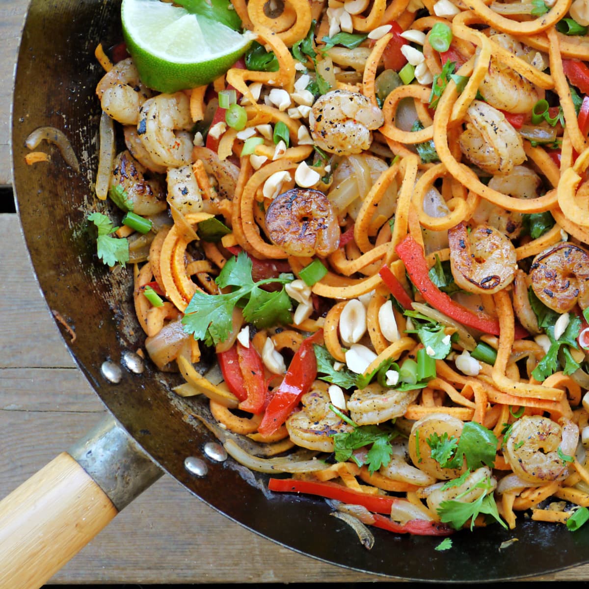 Large wok with sweet potato noodles, vegetables, and shrimp. Garnished with cilantro and peanuts.