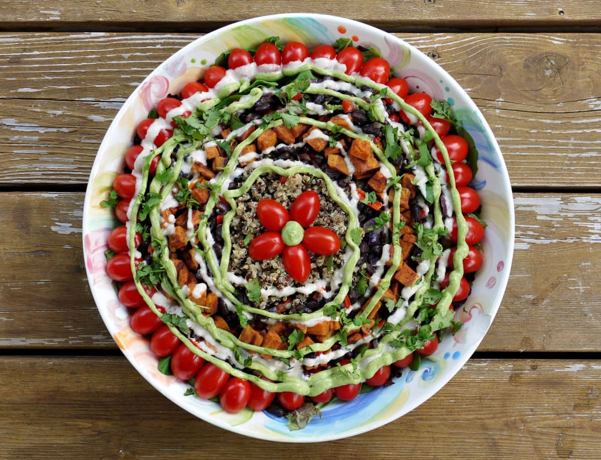 Overhead shot of family-sized salad bowl filled with greens, vegetables, quinoa, and roasted vegetables, dressed with sour cream and avocado dressings.