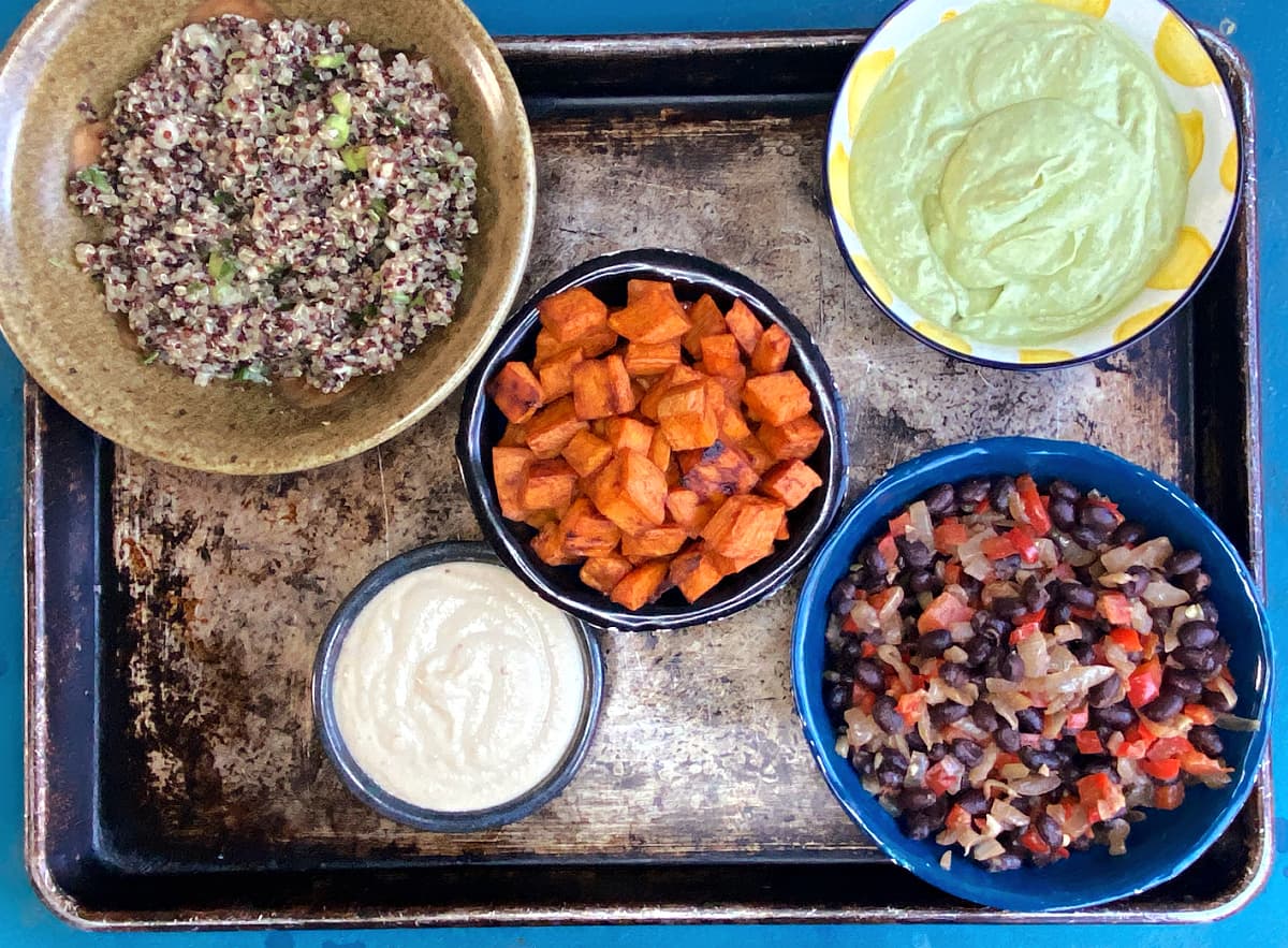 Prepared Cuban salad components: seasoned quinoa, roasted sweet potatoes, cilantro-avocado dressing, cashew sauce, and black beans.