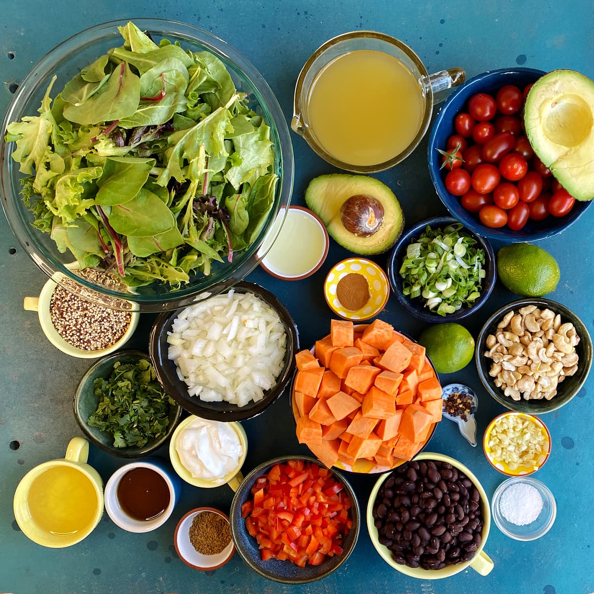 All Cuban Salad ingredients displayed in individual bowls on blue table.