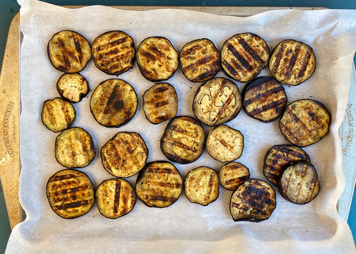 Grilled eggplant slices on parchment, on a baking tray.