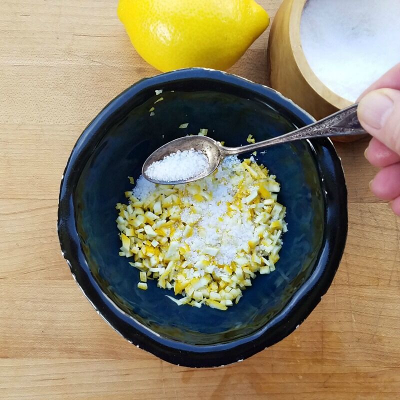 salt being spooned over finely chopped lemon. 