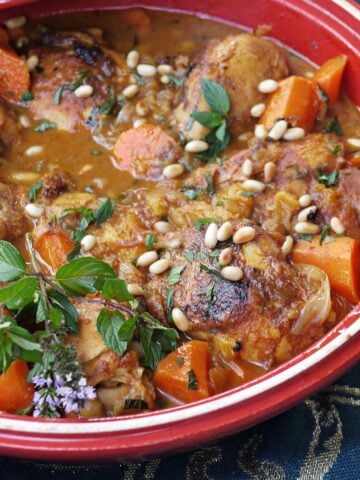 Closeup of Chicken tagine, garnished with fresh herbs and pine nuts.