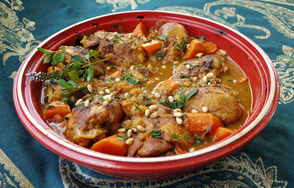 Chicken tagine garnished with mint flowers, pine nuts, and fresh herbs, in the bottom of a tagine pot..