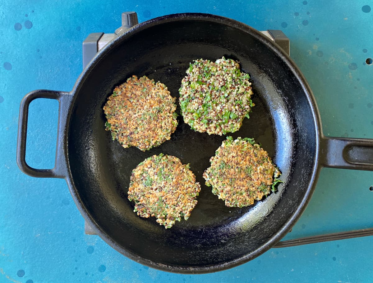 Quinoa fritters frying in a cast iron skillet.