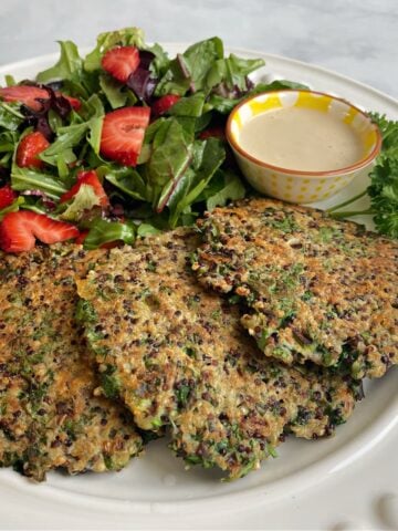 Three quinoa patties plated and served with a strawberry salad.