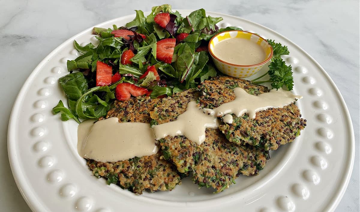Three quinoa patties plated, drizzled with tahini sauce, and served with a strawberry salad. .