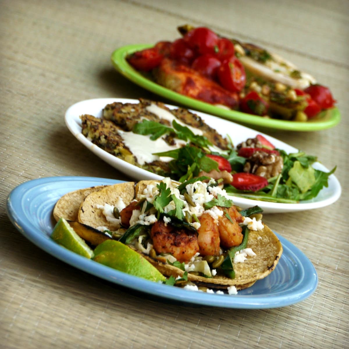 Three plates of food; shrimp tacos in foreground. 