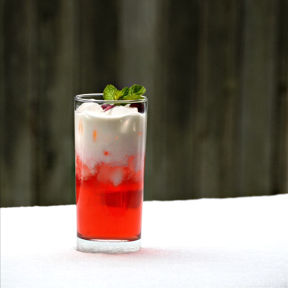 Tall glass in the snow, filled with a bi-colored beverage: white on top, and red on the bottom.