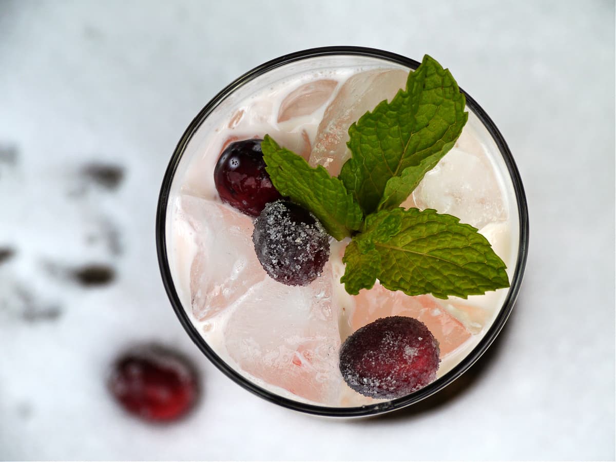 Overhead shot of cream and ice in a glass, garnished with mint and cranberries.