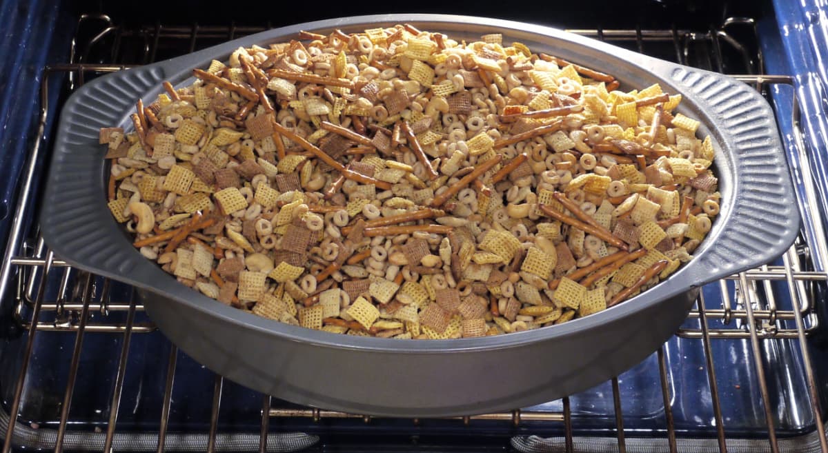 Roasting pan filled with Chex mix, baking int he oven. 