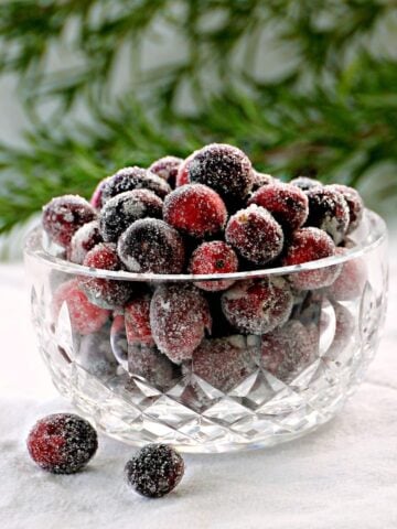 Small crystal bowl of sugared cranberries, with a few berries sprinkled on the table around it.