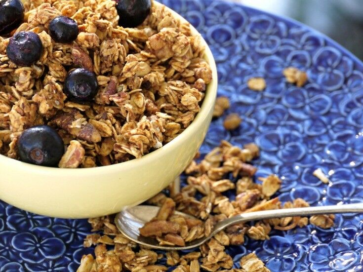 Angled shot of granola in yellow bowl, on blue flowered plate. 