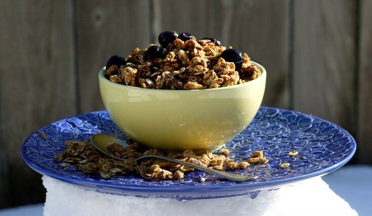 Yellow bowl of granola on blue plate. Granola sprinkled at base. 