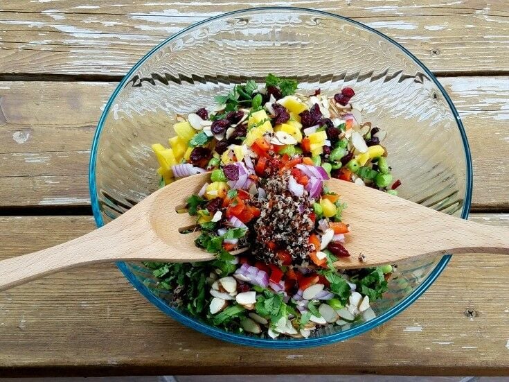 Salad ingredients in glass bowl. Two wooden spoons on either side, tossing ingredients. 