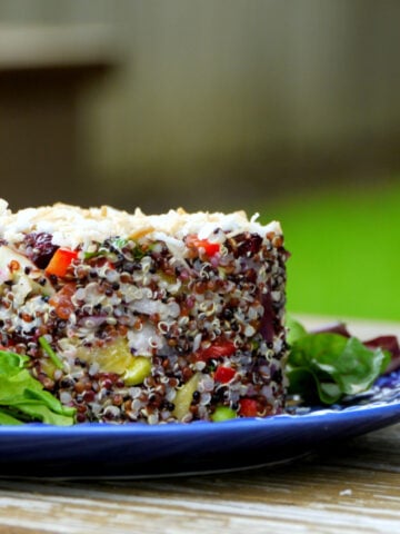 Cylinder-shaped stack of quinoa salad studded with mango, peppers, and edamame, on a plate.