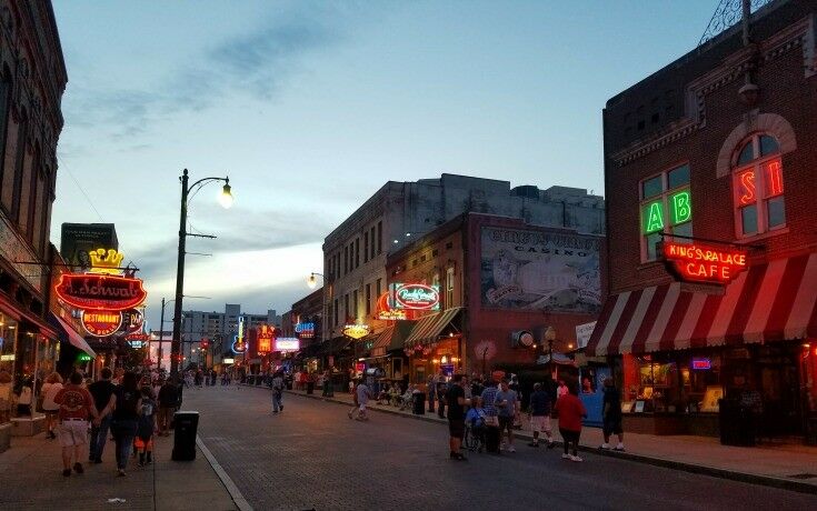 View down Beale Street at twilight: neon signs lighting cafes and bars on either side of street. 