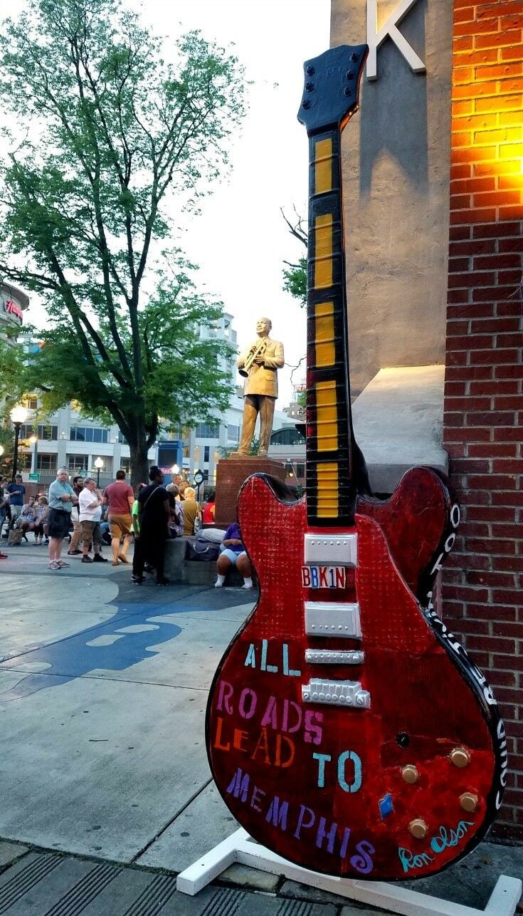 Oversized red Gibson electric guitar, inscribed: All Roads lead to Memphis. Golden WC Handy statue in background. 