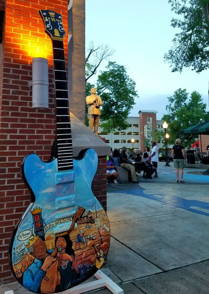 Oversized Gibson with black neck, blue-sky upper body, and scene of Ruby Wilson painted below. 