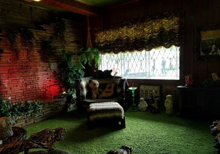 INterior of Graceland's Jungle Room: green shag carpet, dark red mood lighting, silk foliage, and animal motifs. 