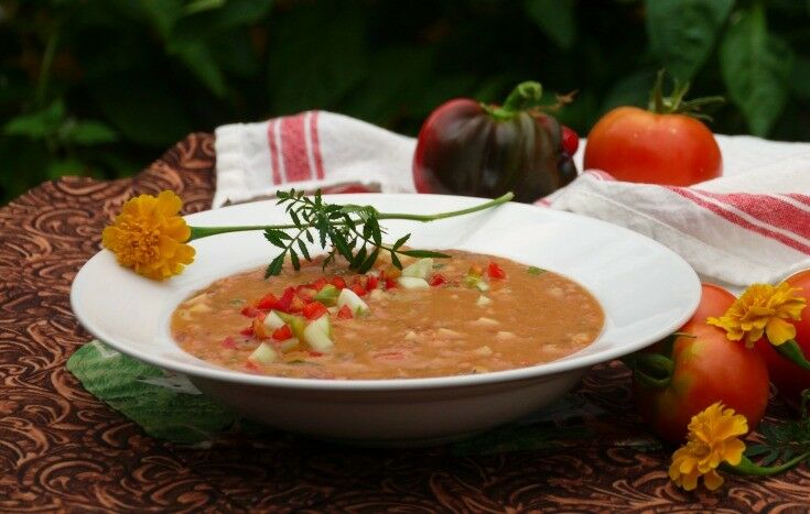 Side shot of soup in bowl, garnished with a marigold. Large tomatoes are in the background. 