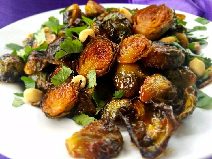 Roasted brussels sprouts on a plate, garnished with fresh cilantro and peanuts. 