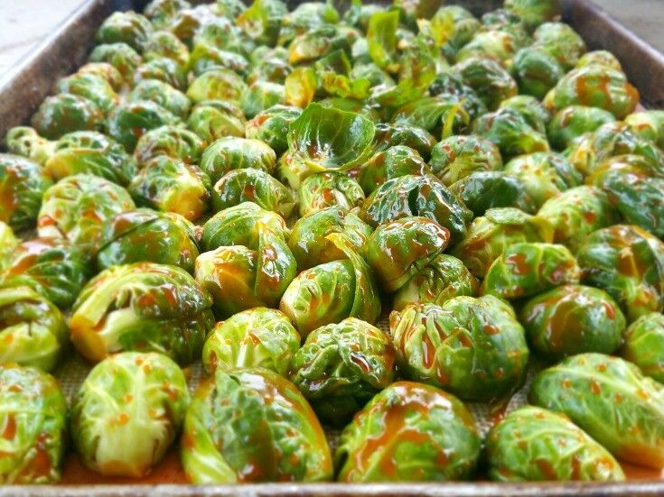 Brussels sprouts dressed with a thin red sauce, arranged cut side down on a sheet pan. 