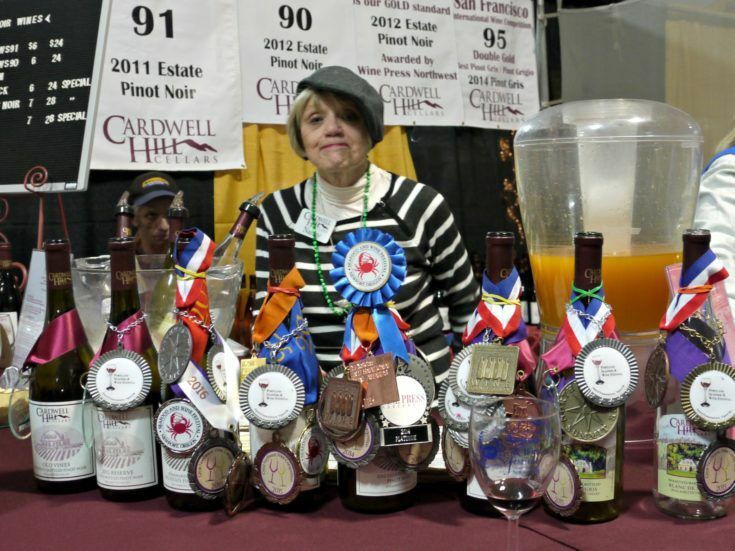 Woman standing behind many bottles of Cardwell Hill Cellars wine, all with multiple award ribbons hanging from them. 
