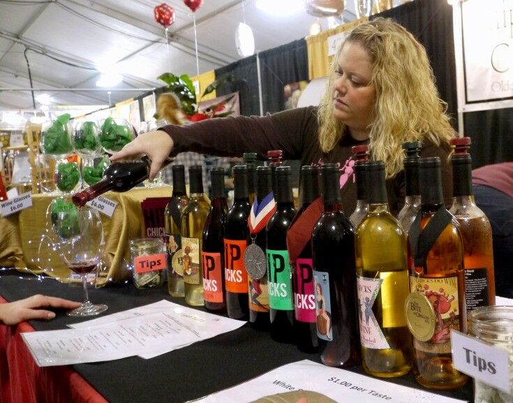 Woman pouring wine, with wine bottles lining counter. 