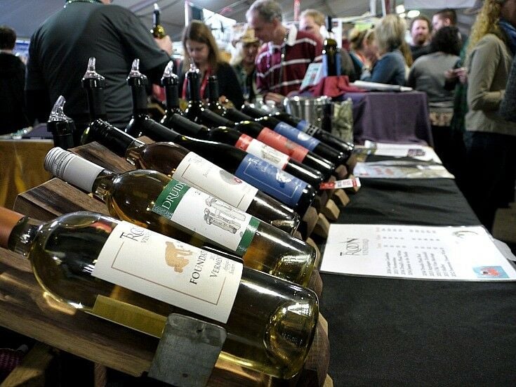 A line of wine bottles with festival attendees milling in the background. 