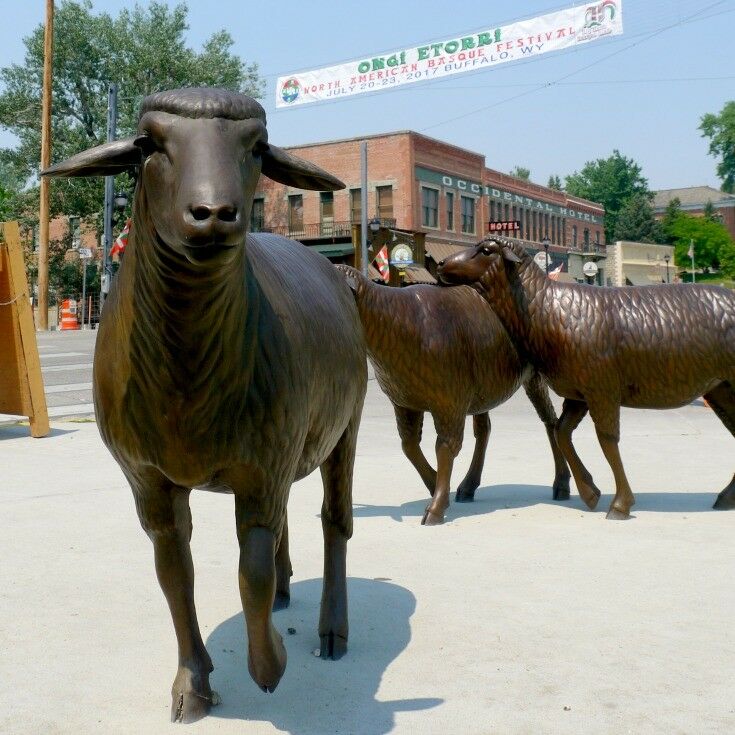 Bronze sheep statues on a street corner in Buffalo, Wyoming. Banner announcing the Basque Festival hangs across the street behind them. 