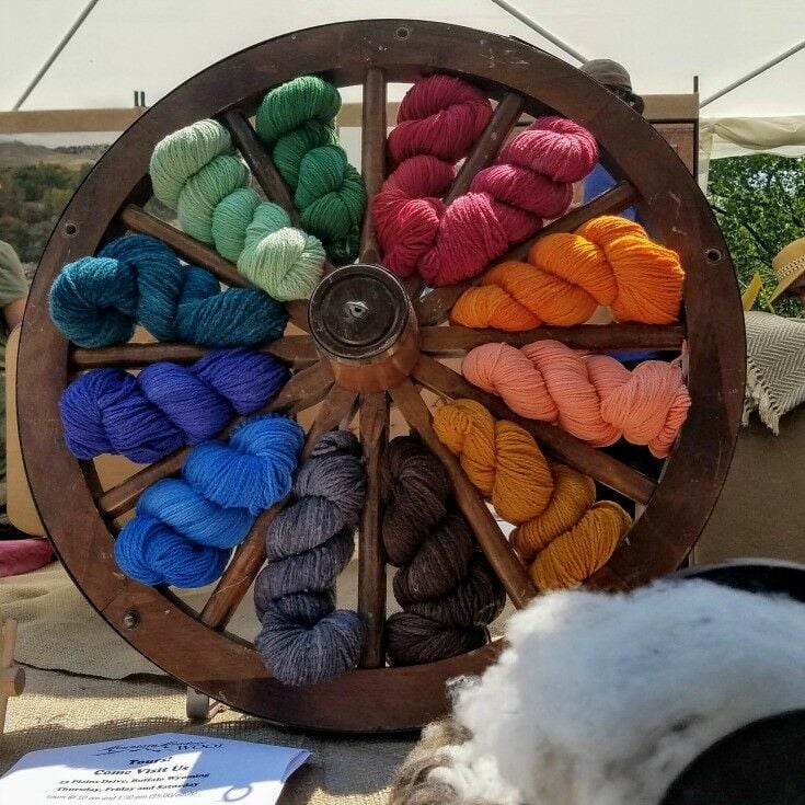 An old-fashioned wagon wheel with skeins of colorful wool yarn fitted in between the spokes. 