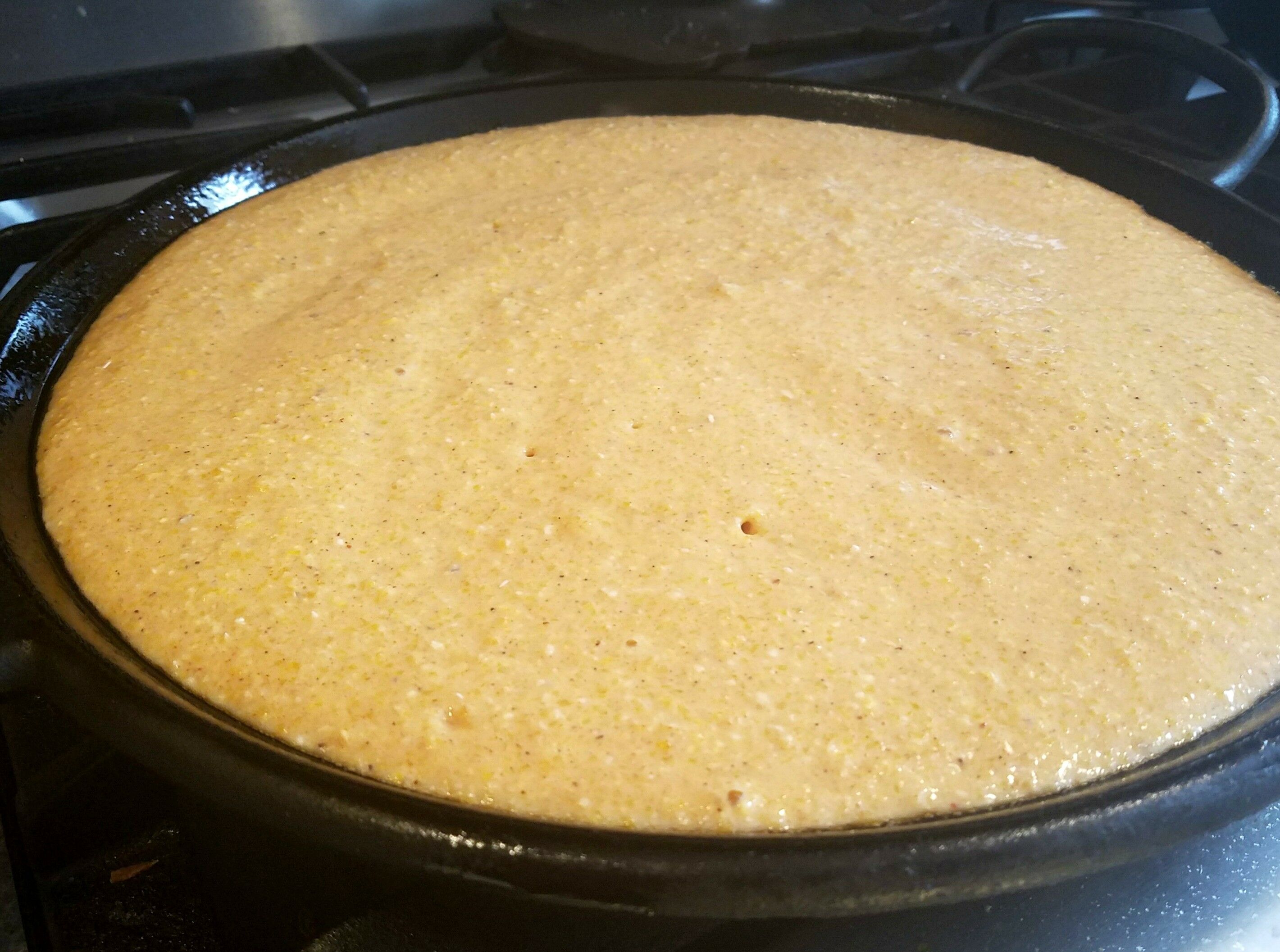 Cornmeal pizza crust poured and cooking on hot griddle.