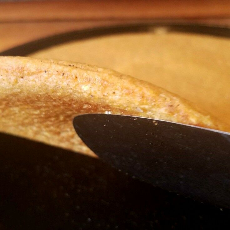 Spatula holding up to show underside of polenta crust. 