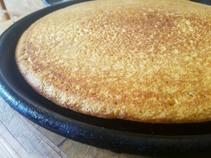 Baked cornmeal pizza crust resting on a cast iron griddle. 
