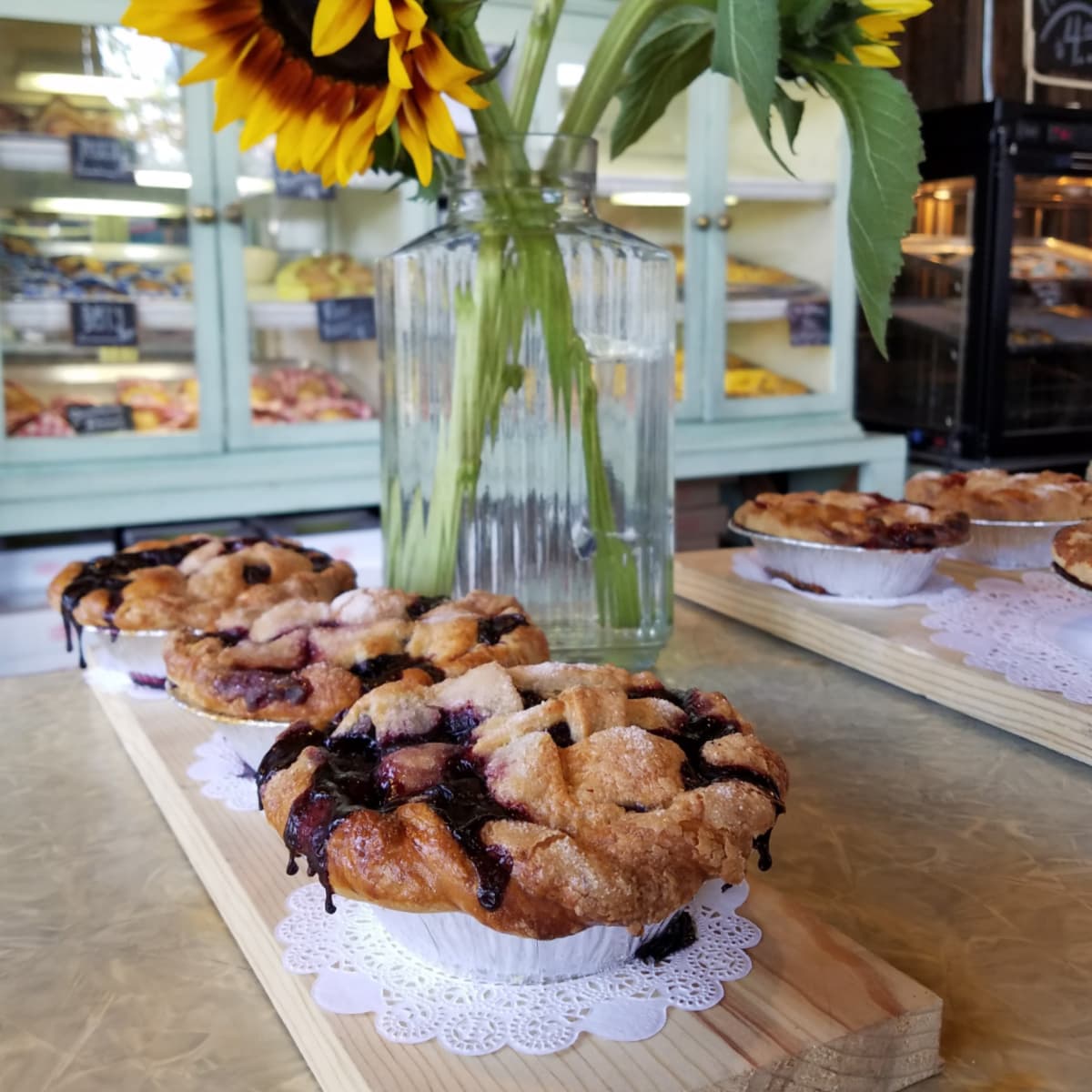 Fresh berry pies on counter, with more baked goods in glass faced cabinets in the background. 