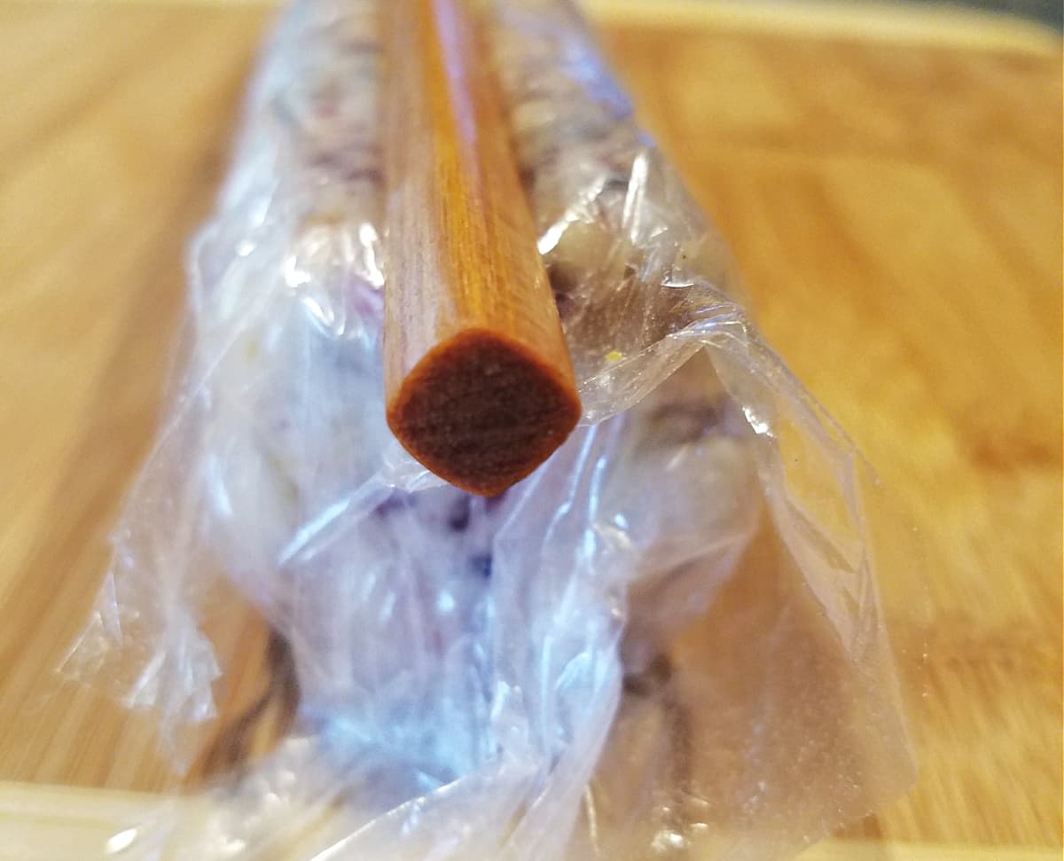 Plastic wrapped dough roll with chopstick on top. 