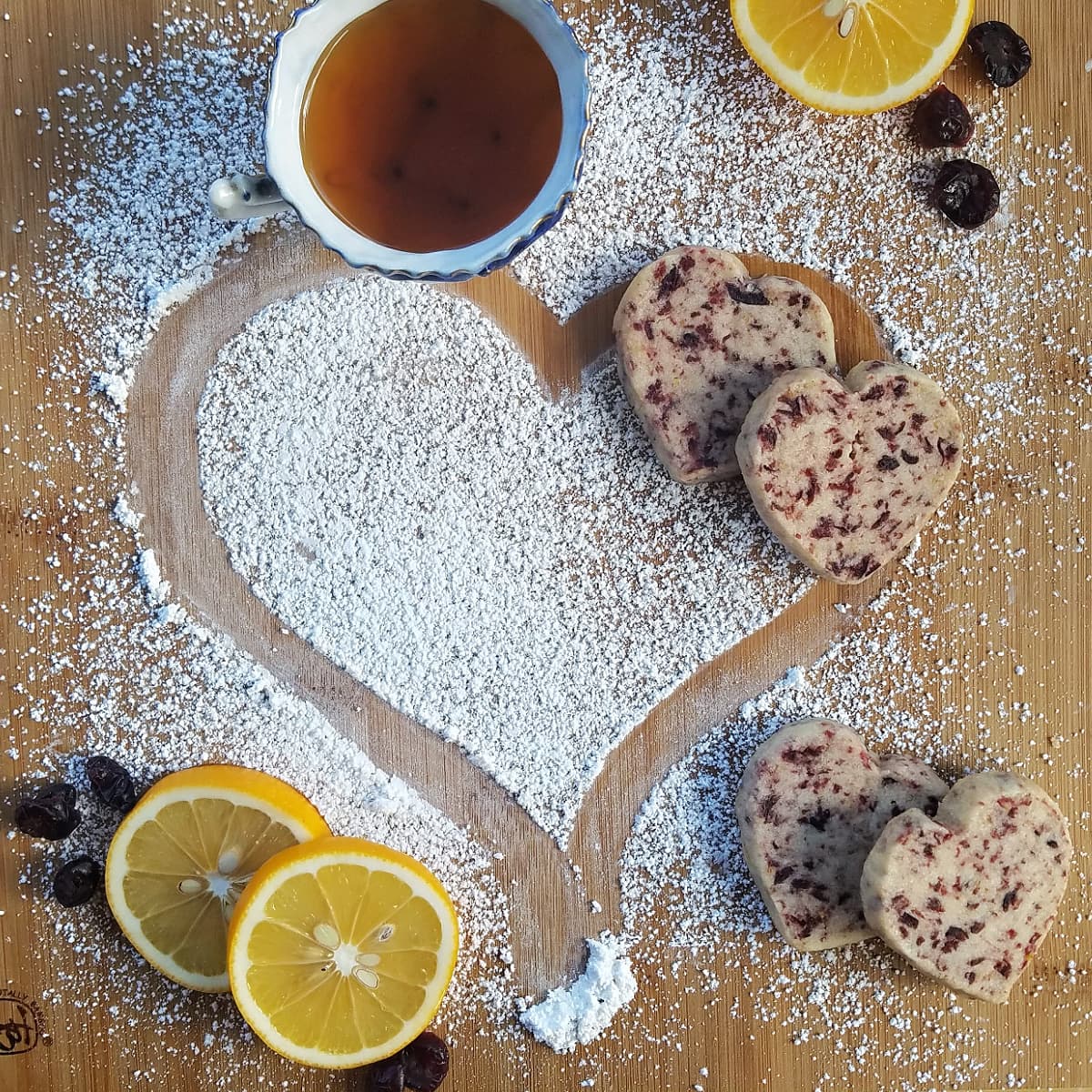 Overhead shot of cookies on a cutting board, with slices of lemons and a cup of tea.