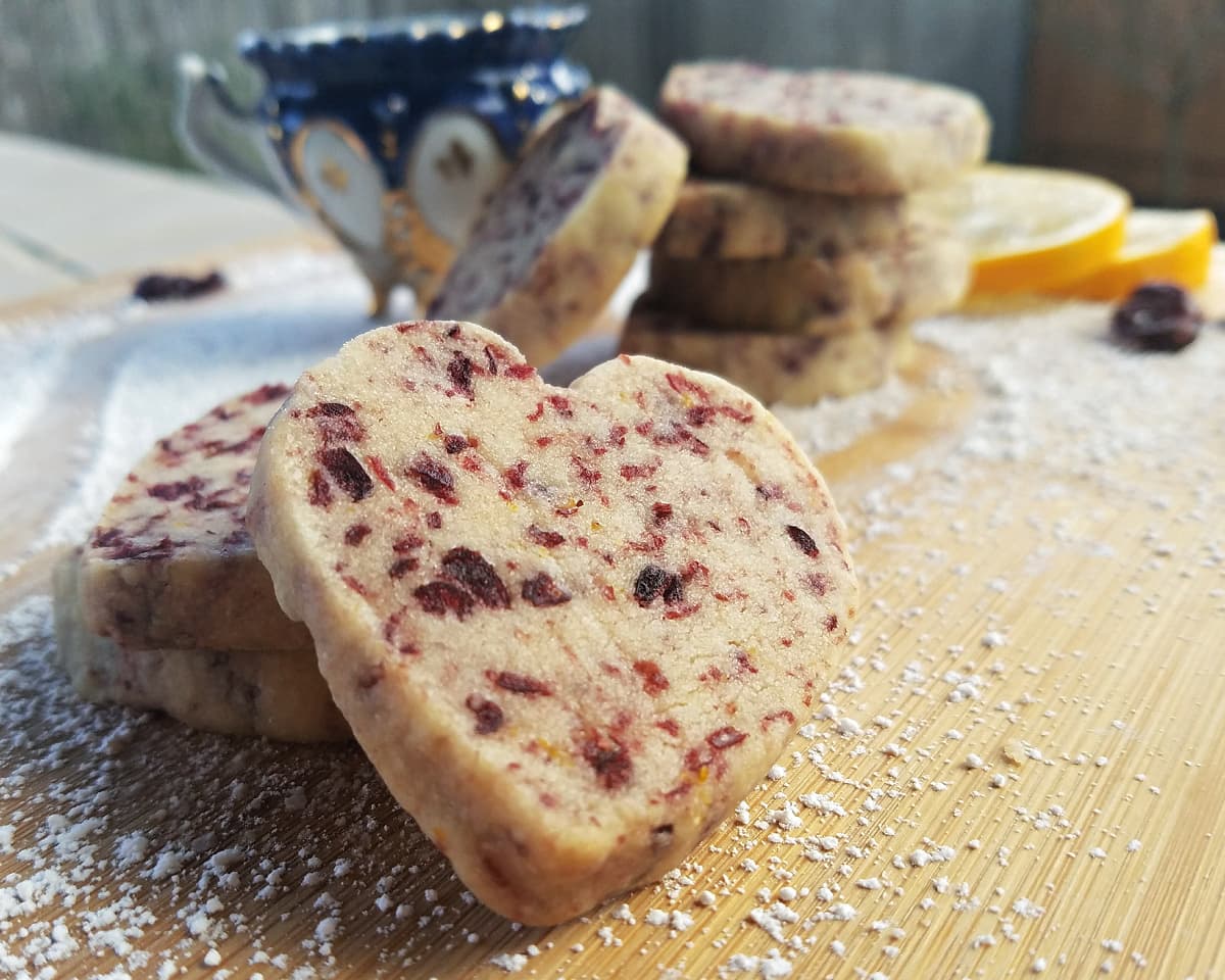 Close-up of heart-shaped shortbread cookies, stacked on a cutting board.